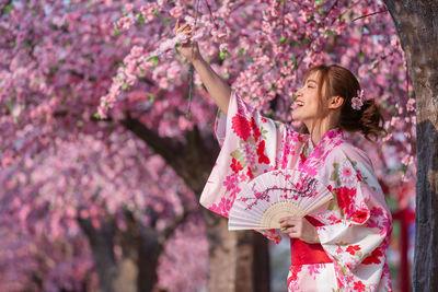 Woman standing by pink cherry blossom tree