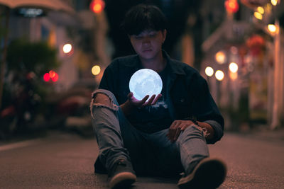 Portrait of man sitting in illuminated city at night