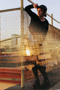 Low angle view of young man standing by chainlink fence