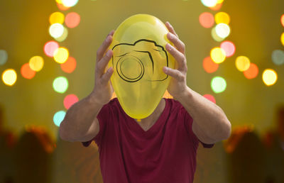 Young holding yellow balloon in front of head with bukeh background blurred