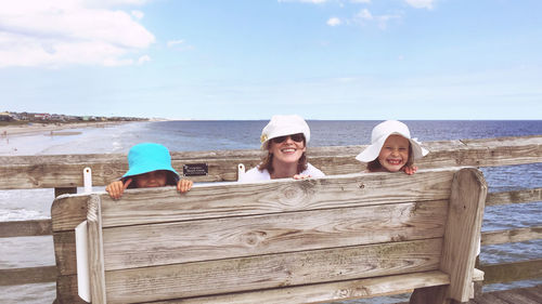 Three females hiding behind a bench on an ocean pier