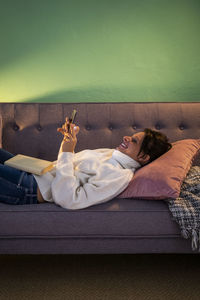 Woman using smart phone while lying down on sofa at home