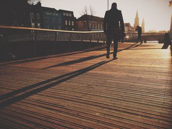 Low angle view of man walking on boardwalk during sunny day in city