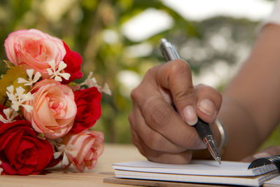 Cropped image of woman writing on book by roses at table