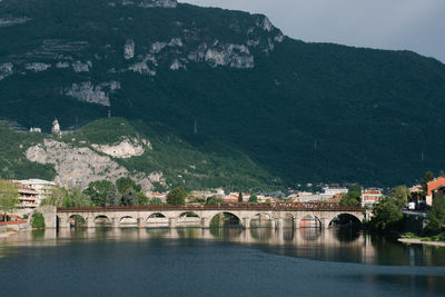 Bridge over river by buildings against mountains