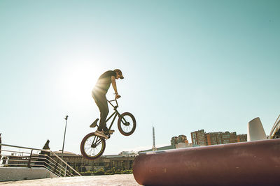 Man riding bicycle on red metallic pipe against sky