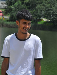 Portrait shot of a indian young guy standing and smiling beside of lake with wearing white t-shirt