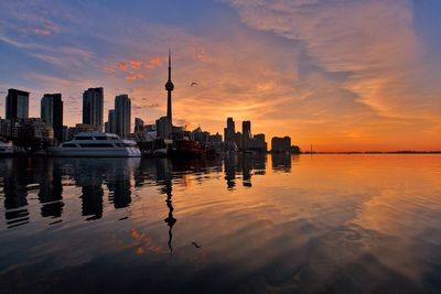 City buildings by sea against sky during sunset