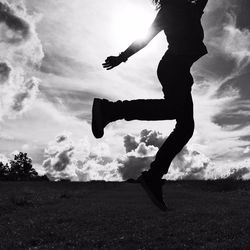 Silhouette low section of girl jumping on landscape against sky