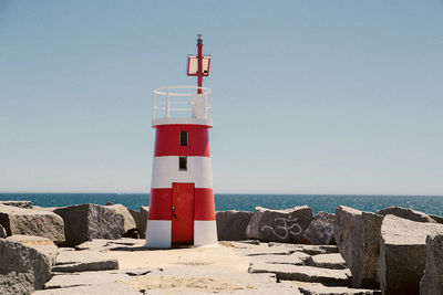 Lighthouse by sea against clear sky