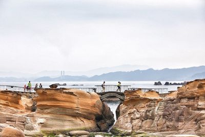 People on rock by sea against sky