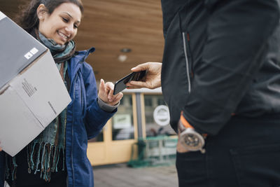 Smiling woman using smart phone to sign for her delivery from messenger