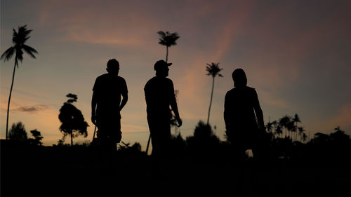 Silhouette people standing by palm trees against sky during sunset