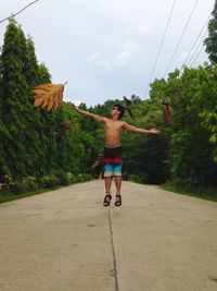 Shirtless young man catching leaves on road