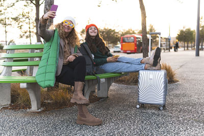 Happy mother with daughter taking selfie though smart phone sitting on bench