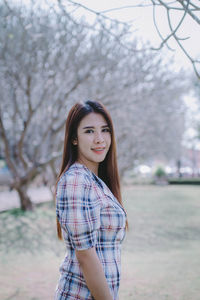 Portrait of young woman standing by bare trees in park