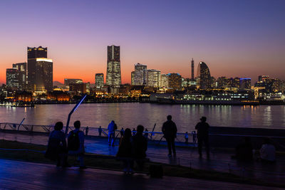 People on river by illuminated buildings against sky in city