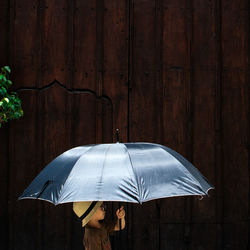 Boy holding umbrella while standing against wooden fence