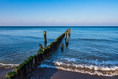 Wooden posts in sea against sky