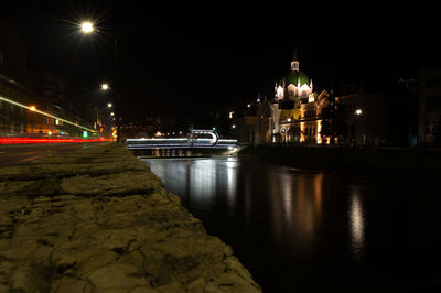 Illuminated city by river against sky at night