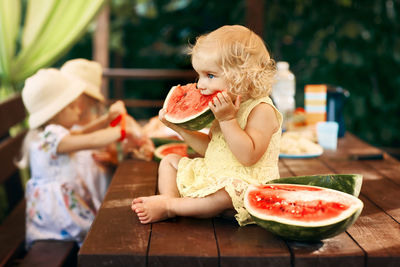 Cute girl eating watermelon while sitting on table