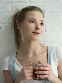 Young woman holding drink while standing against wall