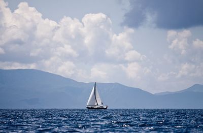 Sailboat sailing in sea by mountains against sky