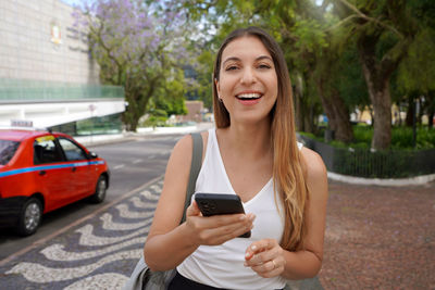 Confident woman holding her mobile phone smiling at camera in porto alegre, rio grande do sul brazil