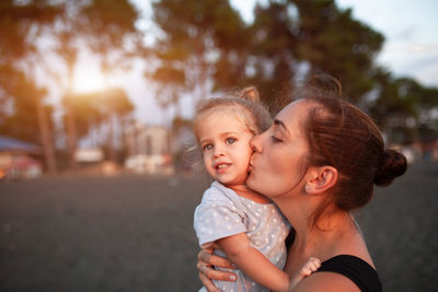 Mother carrying cute daughter while standing in park during sunset
