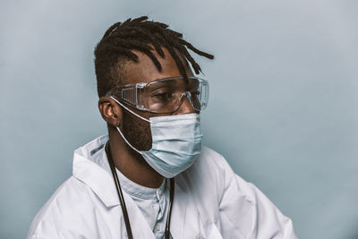 Doctor wearing mask sitting against colored background