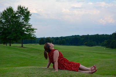 Woman relaxing on grassy field against cloudy sky