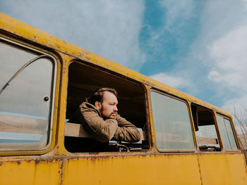 Woman sitting on car window against yellow sky