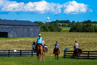 Rear view of people riding horses on field
