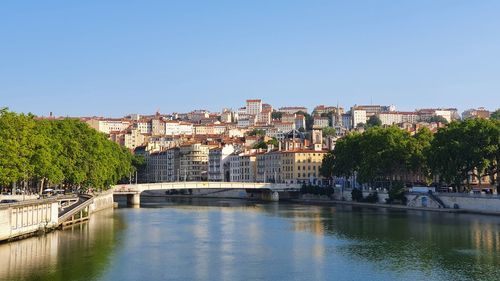 Bridge over river by buildings in city against clear sky