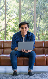 Full length of young man using phone while sitting on sofa
