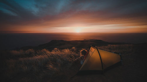 Man sitting in tent during sunset