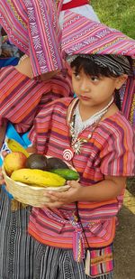 High angle view of girl wearing traditional clothing holding fruits in basket while standing outdoors