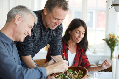 Mature man serving pasta to smiling friend at home