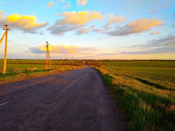 Road amidst field against sky during sunset