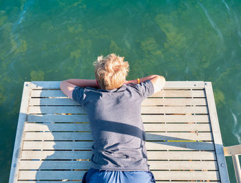 Boy lies on the mole and watches the fish in the lake water below. the joys of childhood