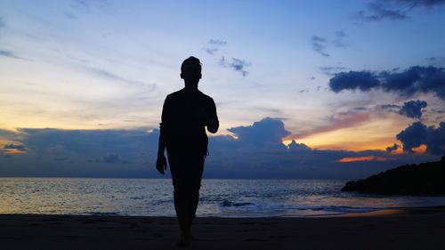 Silhouette man standing on beach against sky during sunset