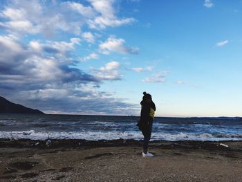 Rear view of woman standing on beach against sky
