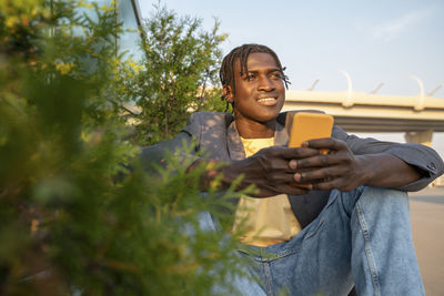 Smiling businessman holding mobile phone by plant