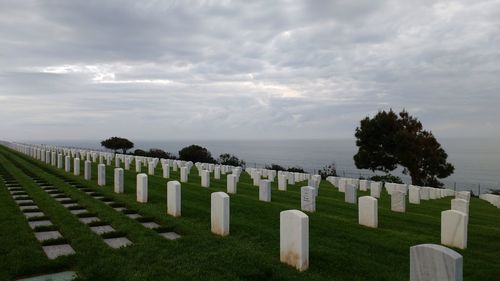 Tombstones on grass by sea against sky at cemetery