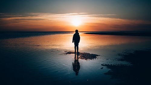 Silhouette man standing on beach against sky during sunset