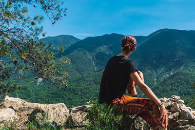 Rear view of woman sitting on mountain against sky