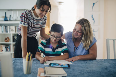 Smiling mother with teenage girl looking at boy studying at table