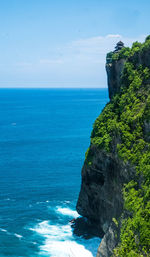 Scenic view of sea by cliff against blue sky