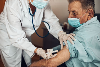 Doctor holding syringe with vaccine and making injection to senior patient with medical mask