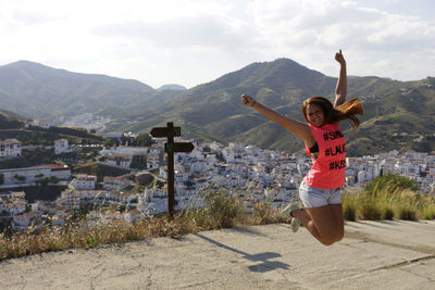 Woman with arms outstretched jumping against mountains and town